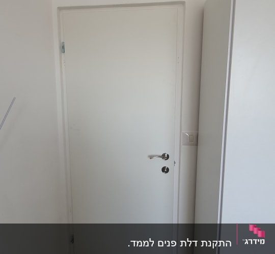 דלת לבנה עם ידית מתכת בחדר קטן